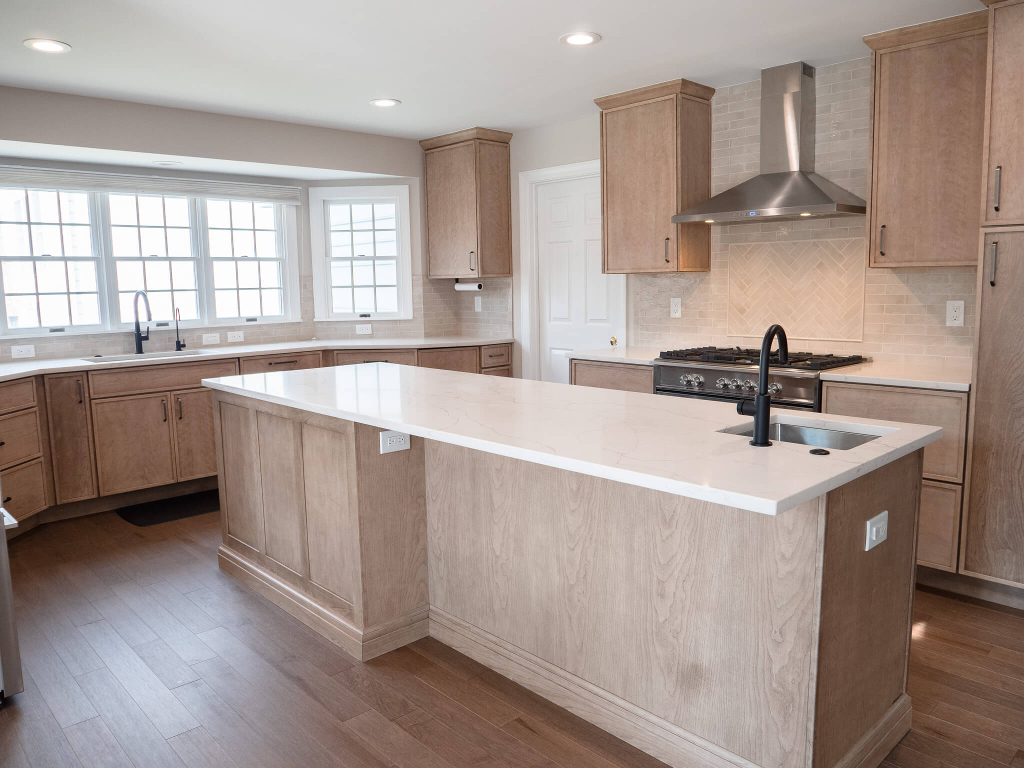 wide-angle showing marble countertop with sink in the middle and the cabinets and hood at the sides