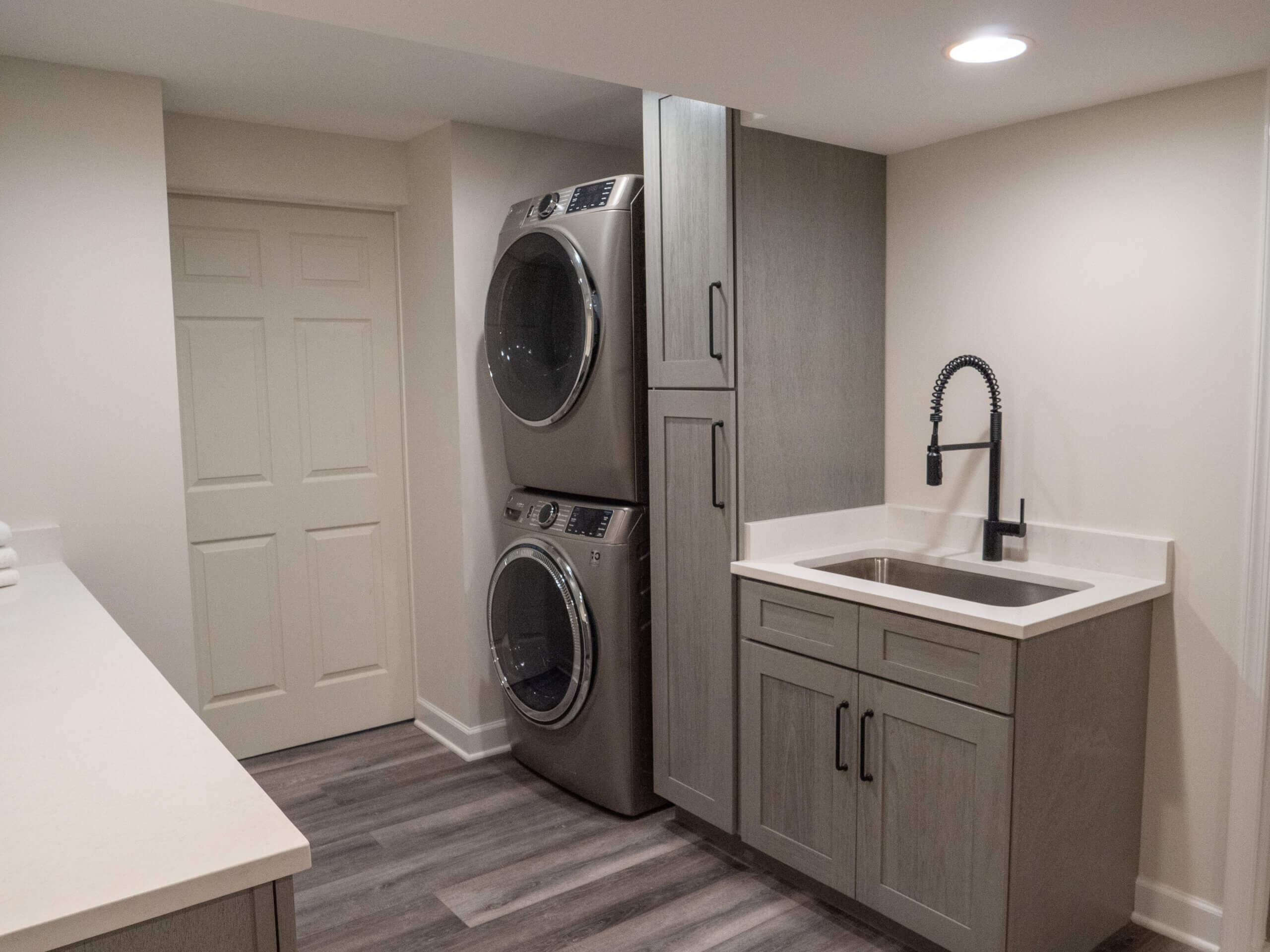 Basement remodeling project with stacked washer / dryer next to large sink and floor to ceiling cabinetry storage | Gaithersburg MD