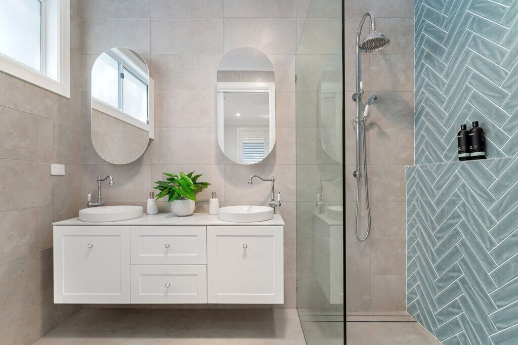 teal-colored bathroom subway tiles in herringbone pattern and double bathroom vanity 
