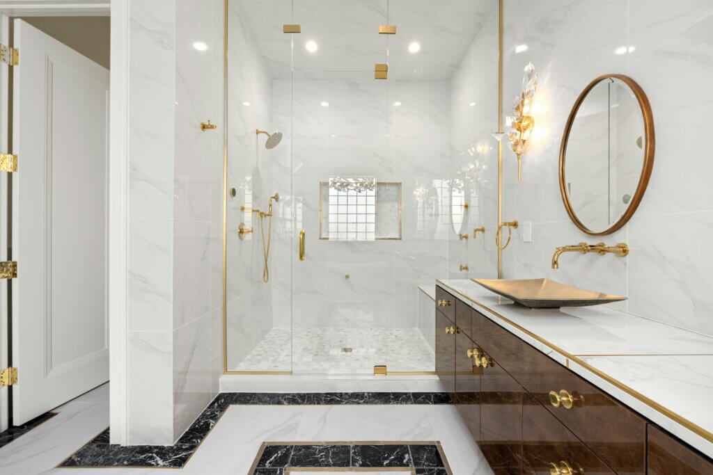 Carrara marble shower tiles in an elegant white bathroom design with gold accent